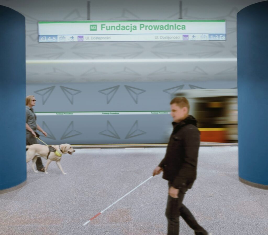 Zdjęcie przedstawia peron metra. Na tabliczce znajduje się informacja, że jest to stacja linii M3: Fundacja Prowadnica. Na pierwszym planie widoczny jest Dawid, który idzie do przodu, badając teren białą laską.