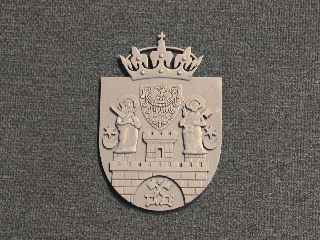 Herb Poznania przedstawia mur z trzema basztami i otwartą bramą. Nad najwyższą wieżą znajduje się orzeł. Na niższych odpowiednio: św. Piotr na lewej i św. Paweł na prawej