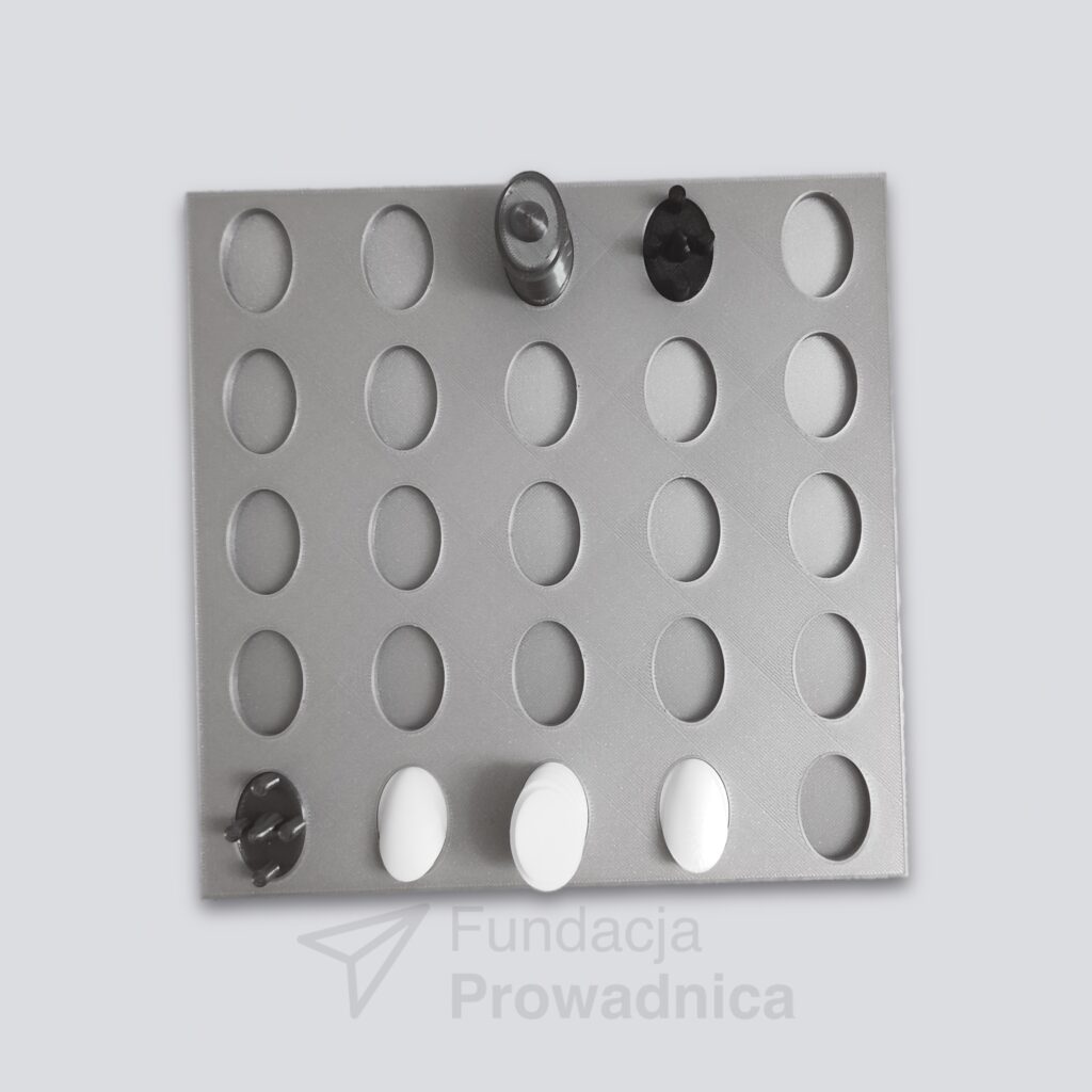 Plansza z owalnymi polami. W kilku polach znajdują się czarne i białe pionki. Czarne są oznaczone wypukłym czubeczkiem.