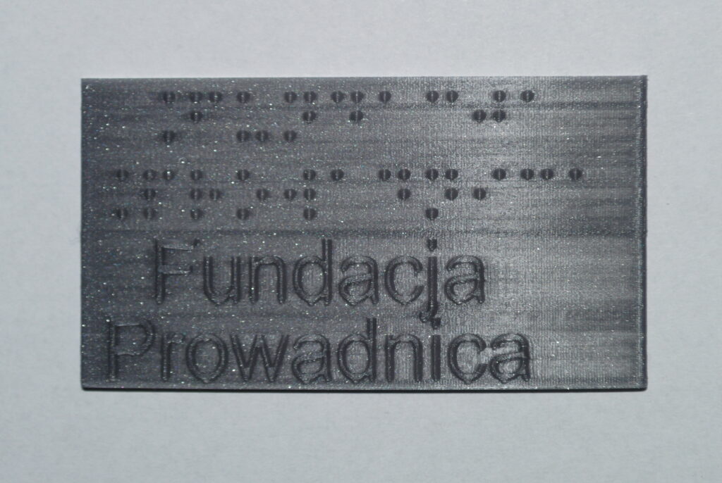 Tabliczka z szarego PLA, z brajlowskim napisem "Fundacja Prowadnica"