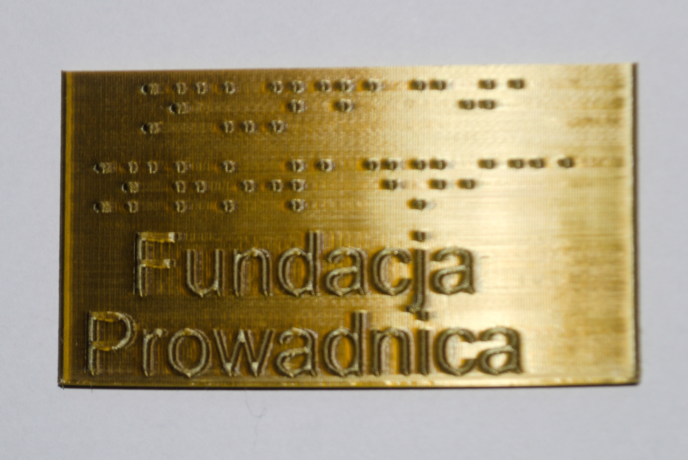 Tabliczka z PLA domieszkowanego mosiądzem, z brajlowskim i czarnodrukowym napisem "Fundacja Prowadnica"