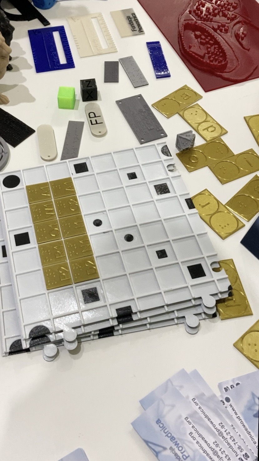 Targi Dostępności. Na stole znajdują się Scrabble z ułożonym napisem Fundacja Prowadnica oraz domino.
