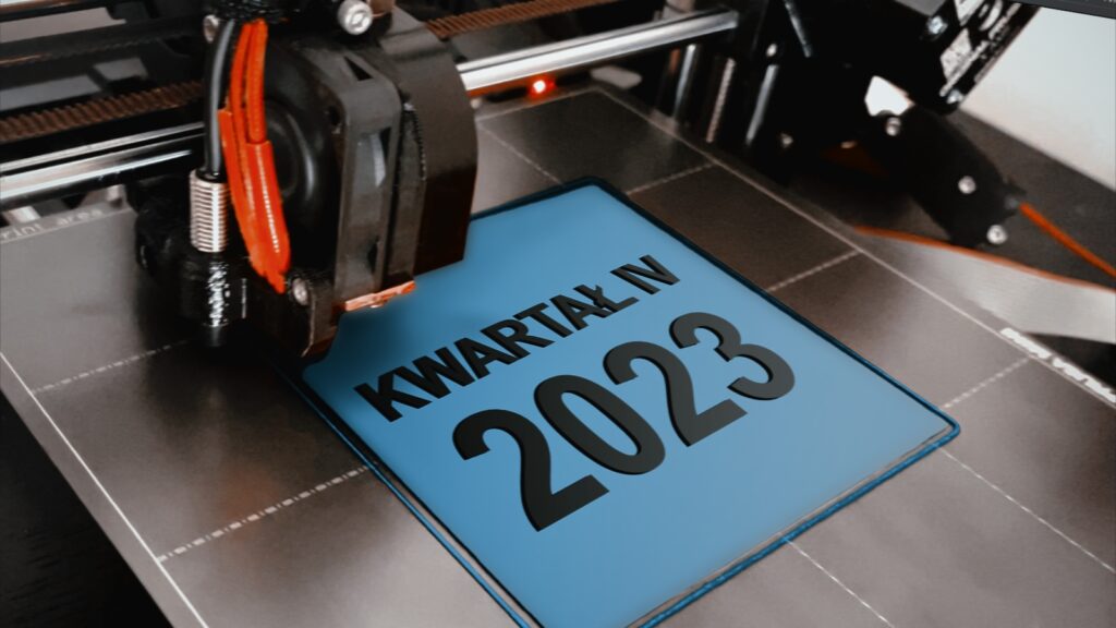Bogusia, drukarka Prusa Mini+, drukuje niebieską tabliczkę z wypukłym czarnodrukowym napisem „Kwartał IV 2023”